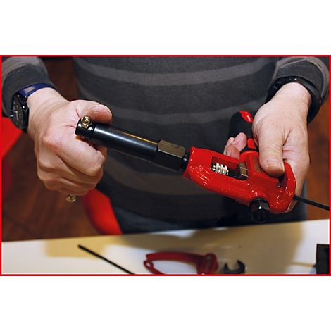 Person hält ein rotes Werkzeug, das Metallrohre verbindet. Das Werkzeug ist in Detailansicht.